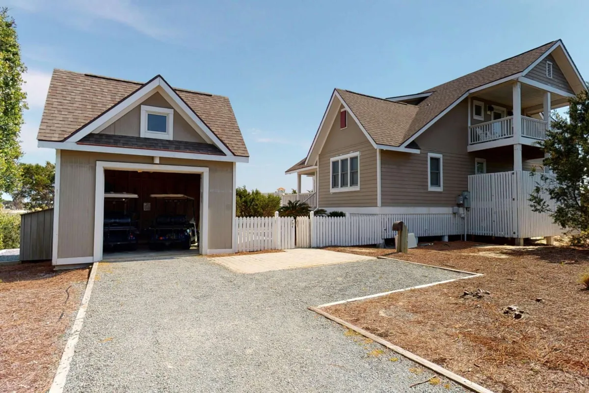 The main house is shown with a fenced yard, front porch, and visible green space, inviting for families and their pets. The welcoming exterior hints at a relaxed atmosphere with room for outdoor activities or unwinding in the yard after a beach adventure.