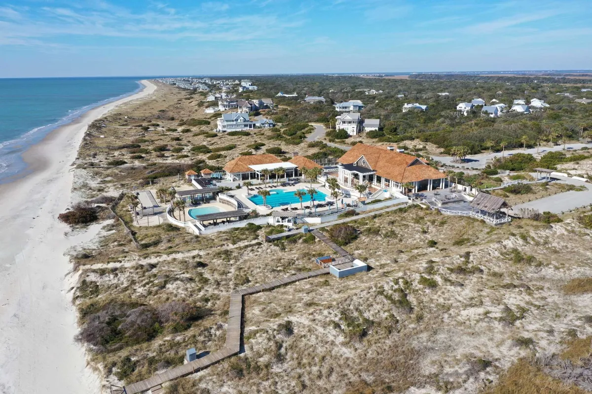 A stunning exterior view of a large pool and spa area overlooking the beachfront, framed by lush landscaping. The calm water of the pool and the ocean beyond create a setting ideal for both relaxation and recreation, hinting at resort-style amenities.