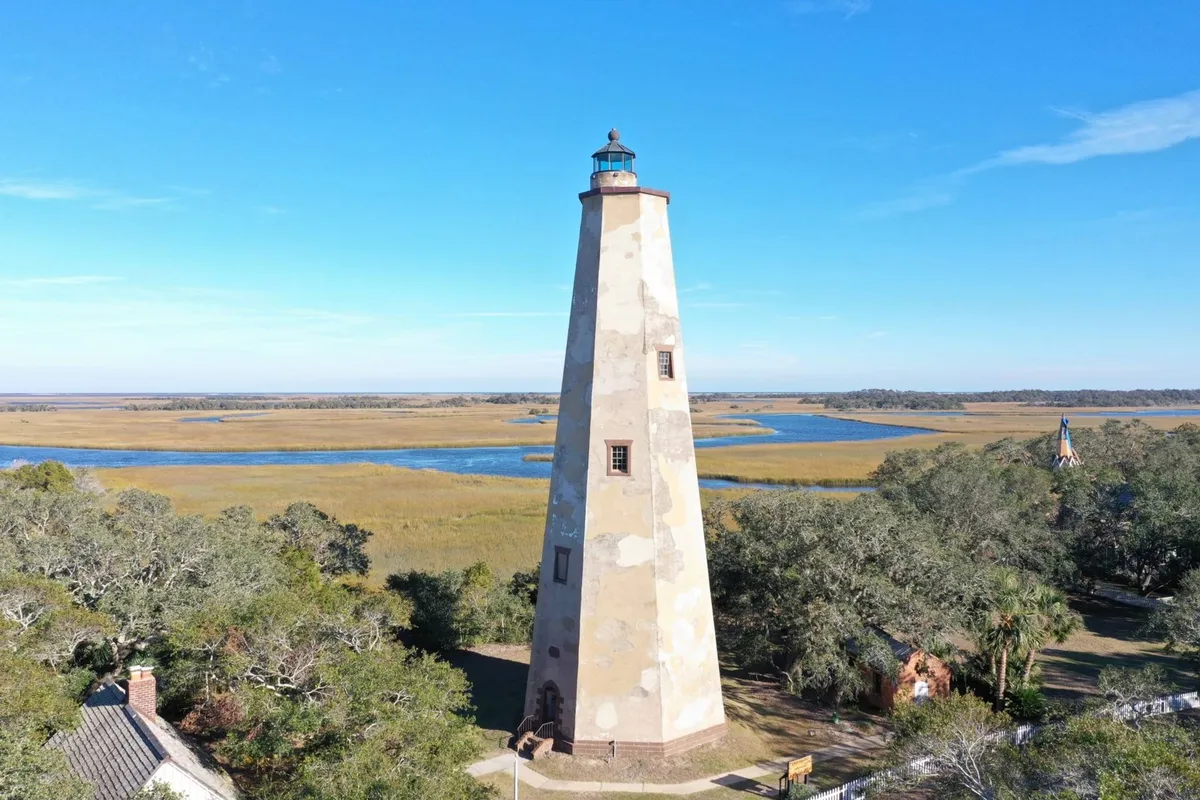 A scenic view of the iconic lighthouse surrounded by marshland and a winding river. The natural landscape invites exploration, bird watching, and photography, tying into the section’s suggestions to climb Old Baldy Lighthouse and explore nature trails.