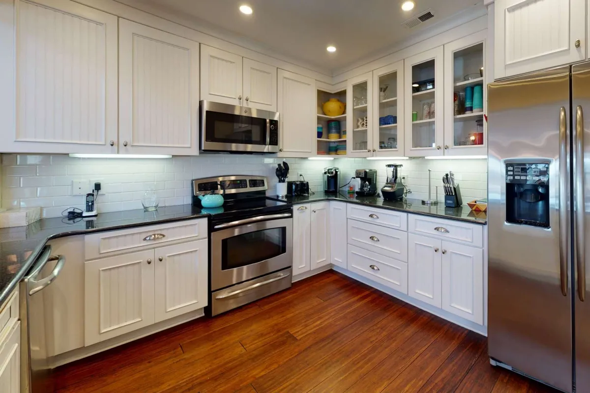 A welcoming, functional kitchen with stainless steel appliances, black granite countertops, and glass-front cabinets filled with colorful dishware. The layout is open and inviting, clearly designed for both serious cooking and entertaining. Ample counter space is visible, and the modern appliances suggest thoughtful extras for culinary adventures.