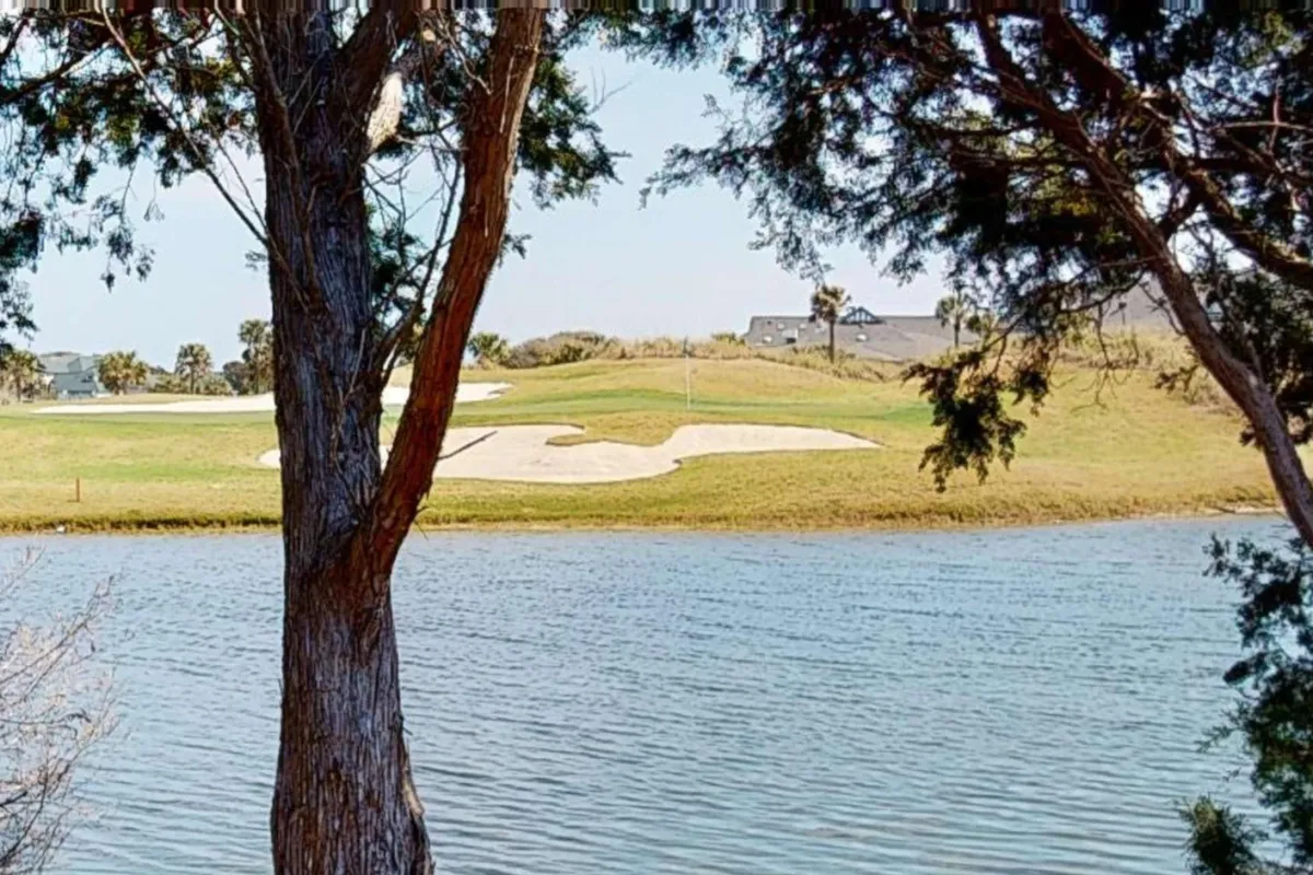 The image presents a sweeping view over a lush golf course with a tranquil water body and surrounding trees. The open expanse illustrates the serene yet inviting environment perfect for golfing and nature walks.