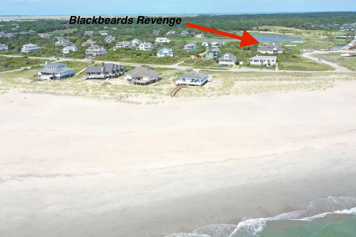 A wide exterior shot of a beachfront property with the shoreline in view, surrounded by other homes and a gentle, open sky. People can be seen engaging in various activities like beach walking, fishing, and enjoying watersports, making the scene feel lively yet relaxed.