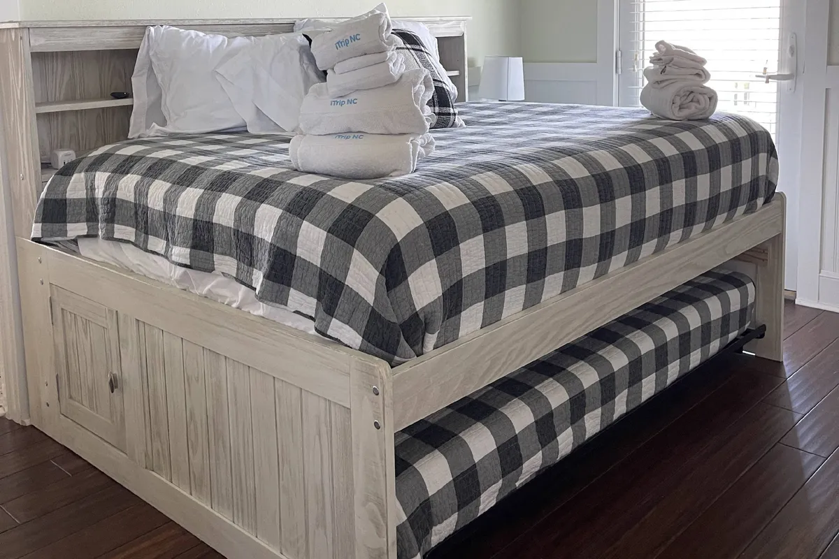 A cozy bedroom with plaid bedding and stacked towels neatly placed on a wooden bed frame. The room feels inviting and comfortable, with soft lighting that suggests a peaceful evening setting ideal for unwinding before bed.