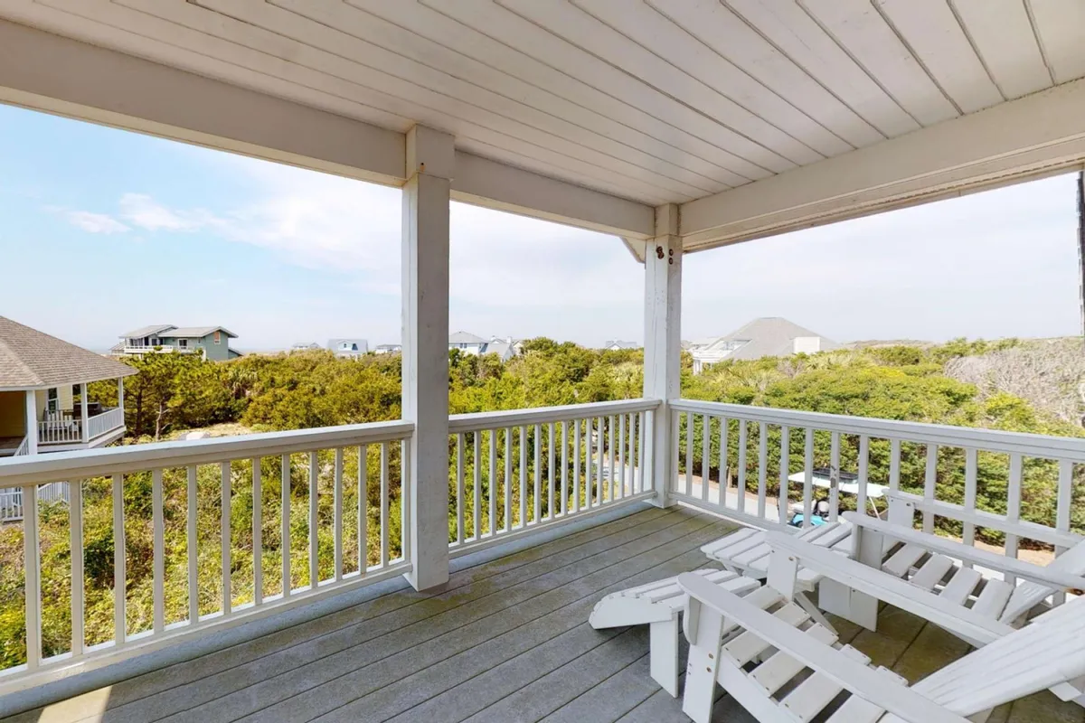 This image features a tranquil deck with Adirondack chairs facing a view of trees and nearby homes, set in an open balcony space. The arrangement evokes a sense of relaxation and invites activities such as enjoying morning coffee, reading, or hosting a small gathering amid fresh island air.