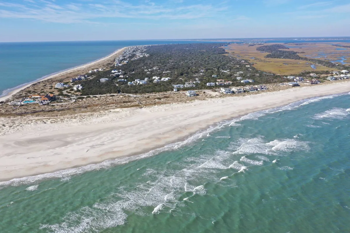 A broad view from above, capturing an expansive coastline, lush greenery, and residential areas, conveying the island's natural beauty and opportunities for exploration. The scene suggests space for sunrise beach walks, nature observation, and a peaceful retreat.